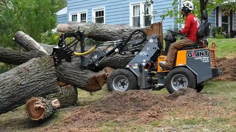 Mini loader moving cut oak logs away from a house after a tree removal in Hermitage, PA